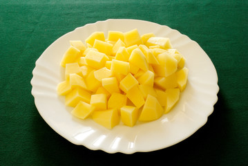 patate crude, tagliate a cubetti, su piatto bianco e tovaglia verde