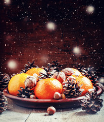 Fototapeta na wymiar Clay plate with orange mandarins, fir cones, walnuts, hazelnuts
