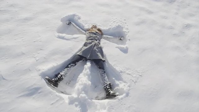SLOW MOTION: Smiling young woman making snow angels