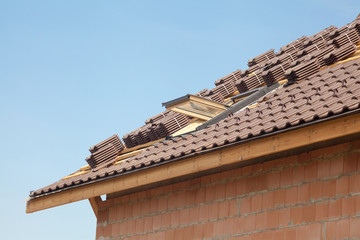 New roof with open skylight, natural red tile against blue sky