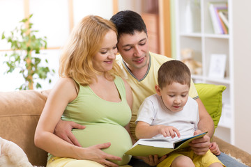 Happy parents reading book to child together on couch in home