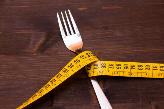 Fork with tape measure on wooden table seen up close