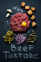 Above view of beef steak tartare on a black wooden background