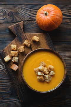 Pumpkin cream-soup with croutons on a wooden cutting board