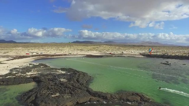 AERIAL: Flying above lots of kitesurfers kiteboarding in flat lagoon