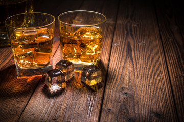 Two glasses of whiskey with ice on wooden table