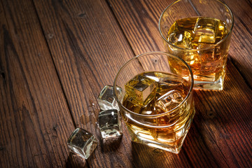 Two glasses of whiskey with ice on wooden table