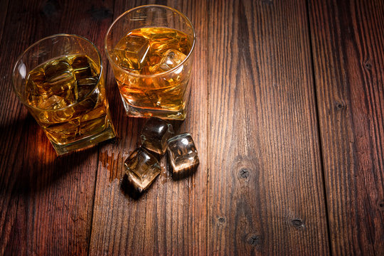 Two glasses of whiskey with ice on wooden table