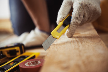 Male carpenter hand holding cutter sitting on the floor with instruments. Concept of home improvement and woodwork. - obrazy, fototapety, plakaty