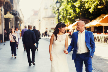 bald groom and bride brunette walking on the streets of the old