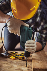 Craftsman in helmet and gloves holding drill at work. Male contractor woodworking with building tools.   - 95024731
