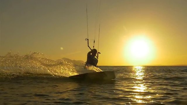 SLOW MOTION: Kiterboarder riding at golden sunset