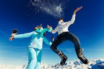 girl and boy in ski suit jump on the background of the Alps Cour