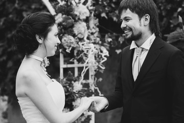 rich stylish happy bride and groom smiling holding hand near a w