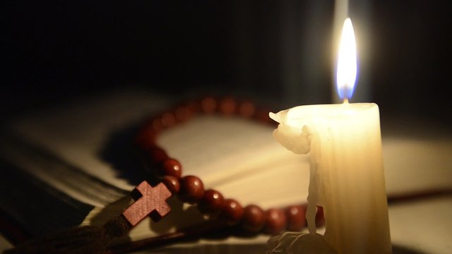 Candle burning on the background of the holy book and a cross