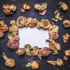 many buds withered roses with petals, laid out around a sheet of paper with text area, vintage style on wooden rustic background top view close up