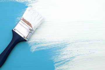 Paintbrush with white paint painting over blue