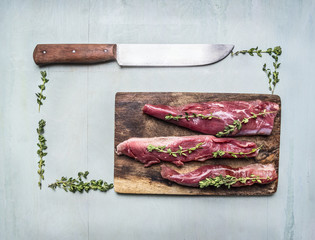 appetizing pieces of raw lamb with herbs and a knife on a cutting board lined rectangle on wooden rustic background top view close up