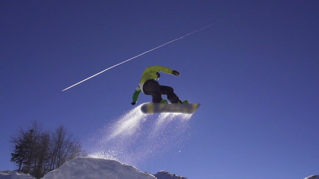 SLOW MOTION: Snowboarder jumps over kicker, low angle view