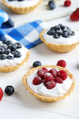 Dessert tartlets with berries on white wooden background
