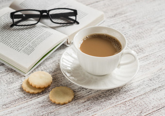 Cup of coffee, biscuits and a book on a white wooden surface