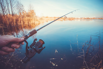 hand with spinning and reel on the evening summer lake