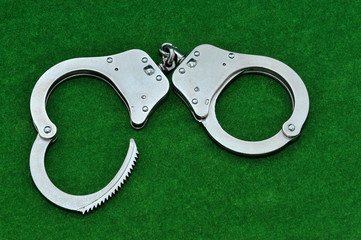 Handcuffs on green background 
