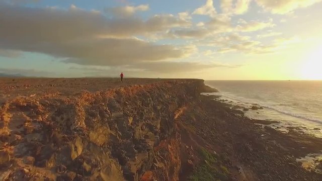AERIAL: Woman jogging on top of ocean cliff at sunset