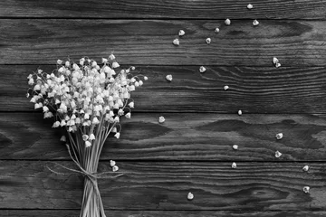 Photo sur Plexiglas Muguet a bouquet of white flowers Lily of the valley and fallen buds on wooden boards in black and white