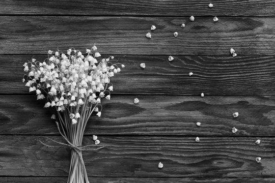 a bouquet of white flowers Lily of the valley and fallen buds on wooden boards in black and white