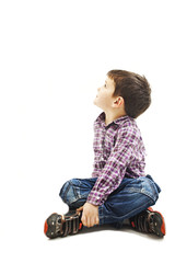 Portrait of a cute little boy sitting on the floor, looking up. Isolated on white background 
