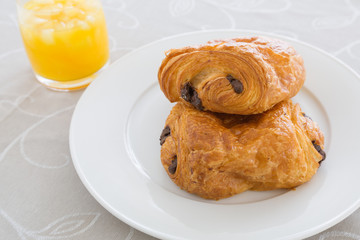 croissants with chocolate filling on a white plate, French pastries with a glass of orange juice in the background. side and top view, backlit, high-key.