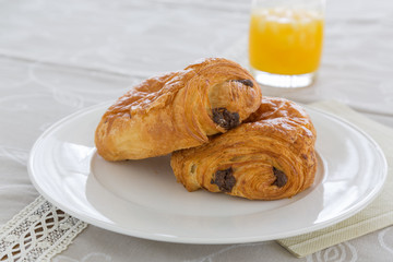 croissants with chocolate filling on a white plate, French pastries with a glass of orange juice in the background. side and top view, backlit, high-key.