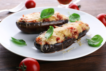 Dish of eggplant with cherry tomatoes and cheese in white plate on wooden table, closeup
