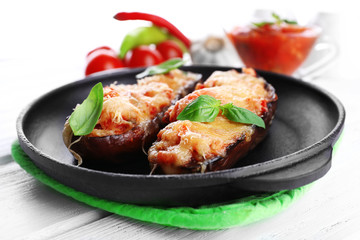 Dish of eggplant with cherry tomatoes and cheese in black pan on wooden table, closeup