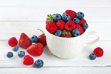 Tasty ripe berries in cup on wooden table close up