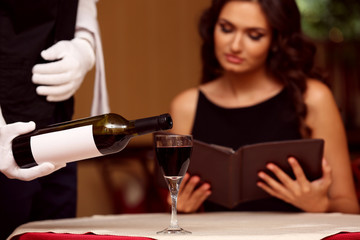 Young pretty lady at the restaurant. Waiter pouring wine in a glass