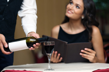 Young pretty lady at the restaurant. Waiter pouring wine in a glass