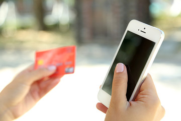 Cellphone and credit card in woman's hands outdoors, close up