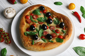 Fresh tasty heart shaped pizza decorated with vegetables and herbs on wooden background