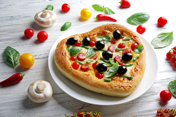 Fresh tasty heart shaped pizza decorated with vegetables and herbs on wooden background