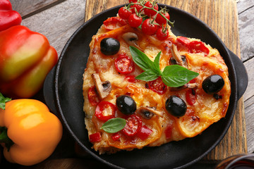 Decorated pizza with vegetables on pan on wooden background