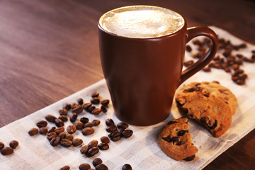 Cup of coffee with roasted coffee beans around and biscuit on cotton serviette on wooden  background, close up
