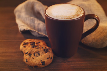 Cup of coffee with milk foam and  cookies with chocolate crumbs on wooden background