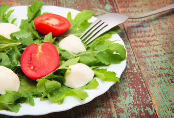 Green salad made with arugula, tomatoes, cheese mozzarella balls and sesame on plate