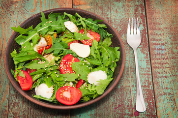 Green salad made with arugula, tomatoes, cheese mozzarella balls and sesame on plate