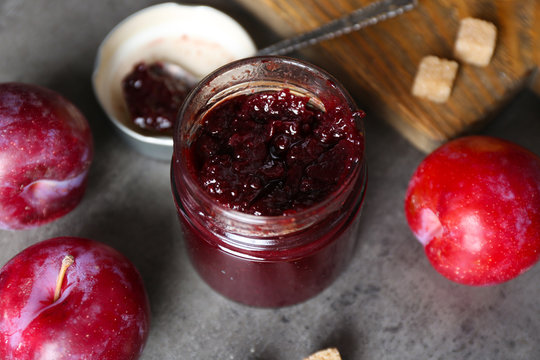A jar of tasty jam, a spoon, plums, crackers and fresh buns close-up