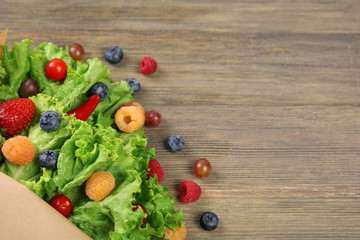 Beautiful bouquet of lettuce and berries in paper sheath on wooden background, close up