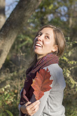 Happy girl holding red autumn leaf in the park