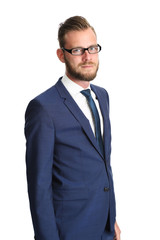A handsome businessman in his 20s standing in front of a white background, wearing a blue suit and tie with glasses. Feeling confident and successful.